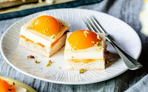Zwei exquisite Stücke spiegeleikuchen mit pudding, garniert mit Pfirsich und Pistazien, auf einem Teller mit einer Gabel.