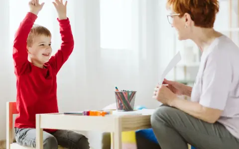 Chłopiec z podniesionymi rękami, uśmiechnięty, podczas sesji terapeutycznej. Może to być pomocne w ocenie objawów ADHD u dzieci test.