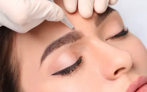 Main d'une esthéticienne réalisant des sourcils permanent effet naturel sur une cliente.