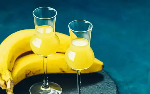 Dwa kieliszki z żółtym likierem bananowym obok dojrzałych bananów. Idealny przepis na domowy likier bananowy.