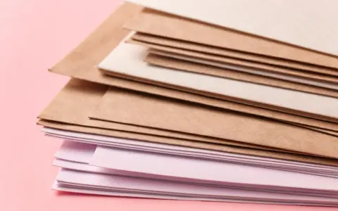 Stos papierów w różnych odcieniach brązu i różu. Różne rodzaje papieru, od kraftowego po delikatnie barwiony, tworzą ciekawą kompozycję.