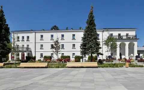 Sanatorium Świt w Solcu-Zdroju, biały budynek z balkonami i łukami, otoczony zielenią i kwiatami.