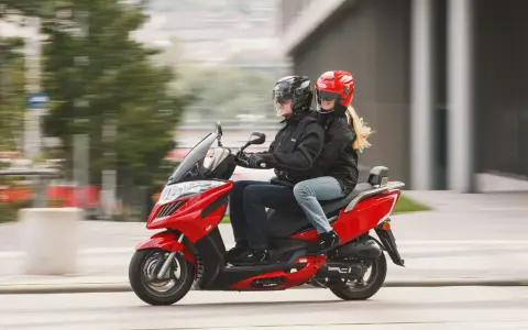 Para jadąca na czerwonym skuterze 125, ubrana w kurtki i kaski, cieszy się jazdą.