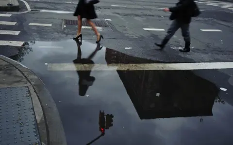 Jay Maisel photography captures a rainy street scene with blurred figures crossing, their reflections distorted in puddles, mirroring the city's mood.