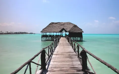 Drewniany pomost prowadzi do chatki na palach na turkusowej wodzie. Idealne miejsce na wiza zanzibar.
