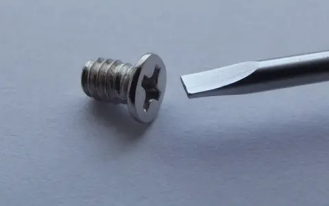 Tornillo metálico con cabeza de estrella y destornillador plano listo para ayudar a como quitar un tornillo pasado.
