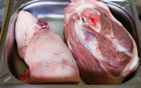 Deux morceaux de viande crue, dont une belle rouelle de porc, reposent dans un bac en métal.