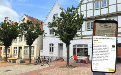 Blick auf die mittelalterliche Itzehoe Altstadt mit Fachwerkhäusern und einem Smartphone, das Informationen über die Stadt anzeigt.