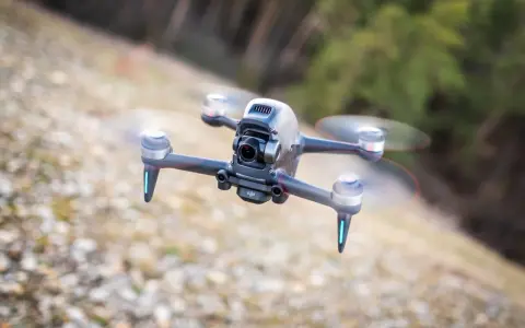 Eine FPV Drohne fliegt über steinigen Boden. Sie hat eine Kamera vorne und leuchtende blaue Lichter an den Armen.