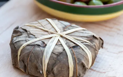 Un mets emballé dans des feuilles séchées, lié par des brins, évoquant les spécialités des Hautes-Alpes.