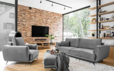 Nowoczesne, szare komplety wypoczynkowe z funkcją spania Black Red White. Wygodna sofa i fotel przy ceglanej ścianie.