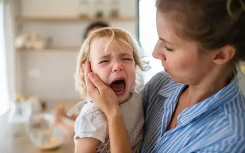 Mama próbuje uspokoić płaczące dziecko, które głośno krzyczy.