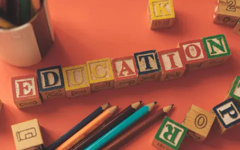 Klocki z literami tworzą napis EDUCATION. Obok leżą kredki i inne klocki, idealne do nauki tekstów po angielsku B2.