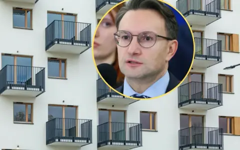 Mężczyzna w okularach przemawia na tle nowoczesnego bloku z balkonami, dyskutując o problemach najmu krótkoterminowego.