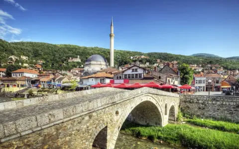Kamienny most nad rzeką, z widokiem na meczet i miasto na wzgórzu. Kosowo atrakcje turystyczne zachwycają.