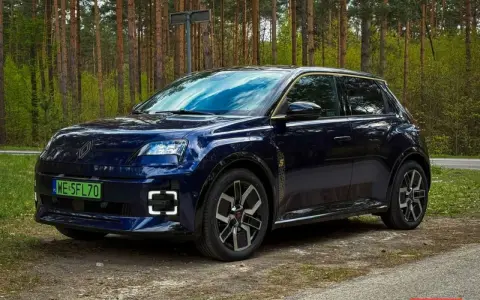 Ciemnoniebieski Renault 5 E-Tech elektryczny stoi na drodze leśnej.