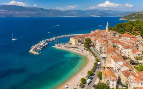Malownicze miasteczko na wyspie Brač z portem pełnym łodzi, plażą i kamiennymi domami pod czerwonymi dachami.