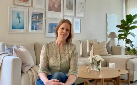 En kvinna sitter i en ljus soffa omgiven av olika inredningsstilar. Tavlor med havstema och en stor grön växt bidrar till den lugna atmosfären.