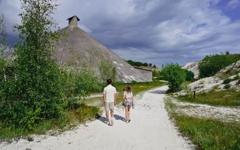 Två personer går på en grusväg mot en stor, konformad byggnad. Omgivningen påminner om vita klippor i Danmark, med grönska och en dramatisk himmel.