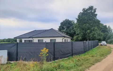 Ciemnoszara siatka na ogrodzeniu panelowym, idealna jako czym zasłonić ogrodzenie panelowe. Dom i samochód w tle.