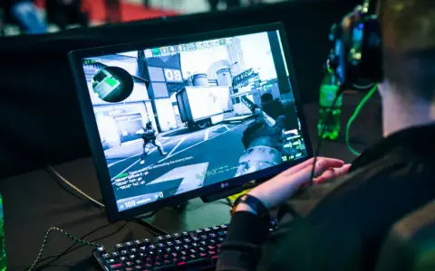 Gracz w słuchawkach gra w CS:GO, próbując jak zmniejszyć ping. Na ekranie widać akcję z gry i klawiaturę.
