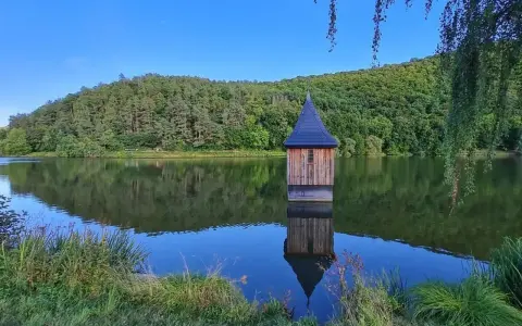 Holzhaus mit spitzem Dach, wie eine kleine Kirche im See, spiegelt sich im ruhigen Wasser.