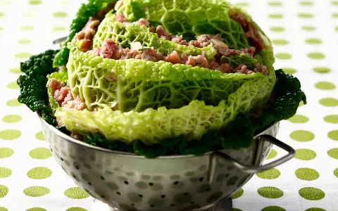 Un chou farci, recette traditionnelle, présenté dans une passoire en métal. Les feuilles de chou vert vif enrobent une garniture de viande hachée.