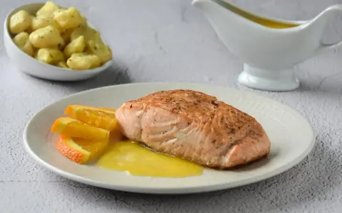 Filete de salmón a la naranja, servido con gajos de naranja y una salsa dorada. Acompañado de patatas pequeñas.
