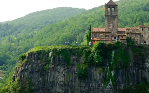 Castillo medieval en un acantilado, uno de los pueblos de Girona, rodeado de vegetación exuberante.