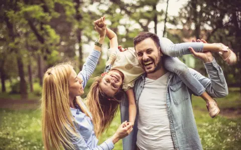Glückliche Familie im Park. Vater trägt Tochter auf den Schultern, Mutter hält ihre Hände. Kein Anzeichen von Einzelkind-Syndrom, nur pure Freude.