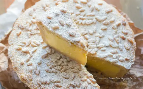 Una fetta di torta della nonna, ricca di crema e cosparsa di pinoli e zucchero a velo, pronta per essere gustata.