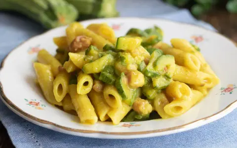 Piatto di pasta penne con zucchine a rondelle e cubetti di pancetta croccante, condita con una salsa cremosa.