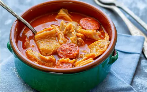 Un cuenco verde con callos a la madrileña, trozos de chorizo y un tenedor.