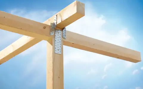 Stabile Holzverbindungen mit Metallwinkeln sichern die Balkenkonstruktion gegen den blauen Himmel.
