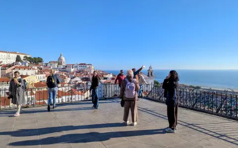 Blick vom Miradouro Portas do Sol auf Lissabons Dächer und das Meer. Touristen genießen die Aussicht.