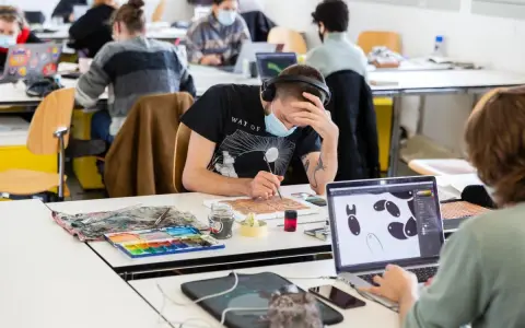 Des étudiants concentrés dans une école d'art, certains peignent, d'autres travaillent sur ordinateur. L'ambiance est studieuse.