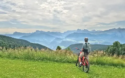 Ciclista con bici da enduro ammira il panorama montano. Un'avventura in bici, forse a Cervia, tra prati fioriti e cime nebbiose.