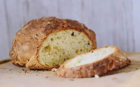 Chrupiący, złocisty bochenek soda bread, z jednym plastrem odciętym, na drewnianej desce.