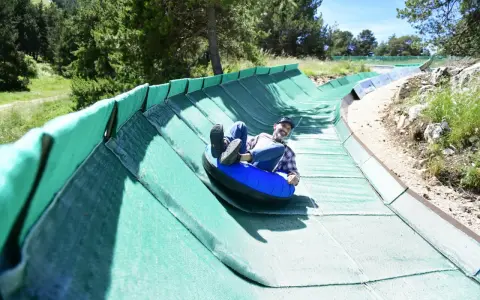 Un homme souriant dévale une piste verte en luge gonflable, profitant des activités Mont Ventoux.
