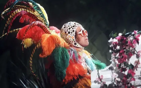 Elton John in einem extravaganten Federkostüm, das an einen Pfau erinnert. Seine ikonischen Elton John Outfits sind legendär.