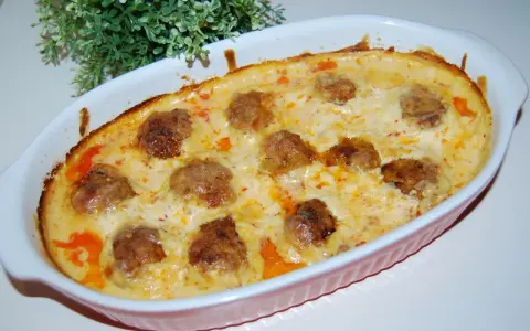 Pulpety w sosie śmietanowo-serowym, zapieczone w naczyniu, z zieloną dekoracją w tle.