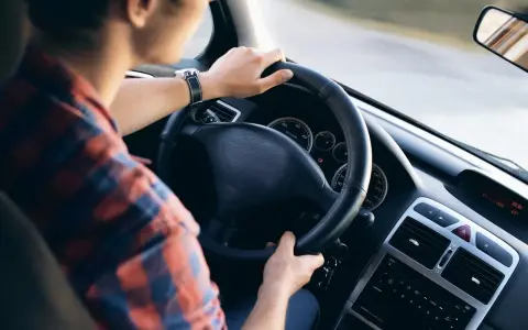 Mężczyzna w kratę prowadzi samochód, wiedząc jak jeździć po wymianie oleju. Na desce rozdzielczej widać zegary i radio.