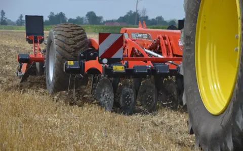Maszyna rolnicza wykonuje bronowanie po orce, spulchniając ziemię i przygotowując pole do siewu.