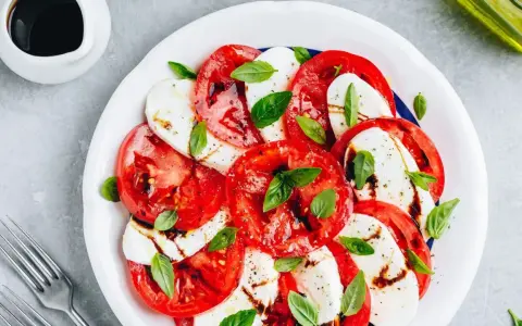 Pyszna sałatka caprese z pomidorów, mozzarelli i bazylii, polana sosem balsamicznym.