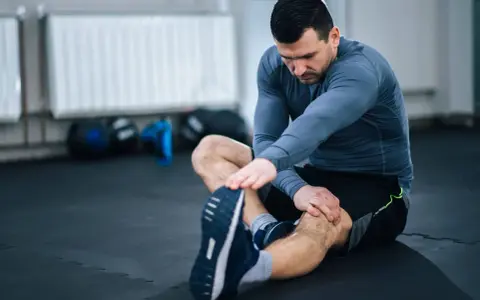 Mężczyzna wykonuje ćwiczenia rozciągające nogi na siłowni, siedząc na macie.