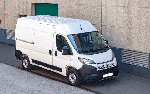 Biały bus dostawczy Fiat Ducato zaparkowany przy betonowej ścianie budynku.