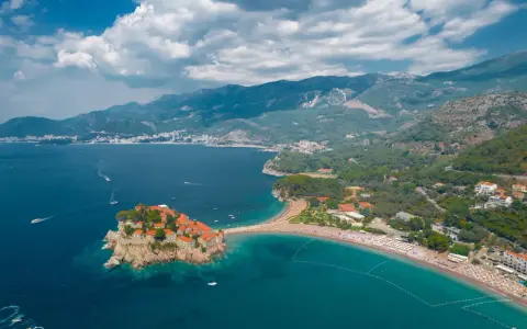 Malownicza wyspa Sveti Stefan, połączona z lądem piaszczystą mierzeją, otoczona turkusowym morzem i górami.