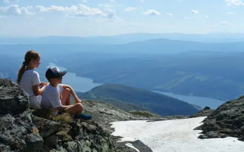 Två barn vilar på en klippa med utsikt över en sjö och berg. Perfekt för vandringsleder i Åre.