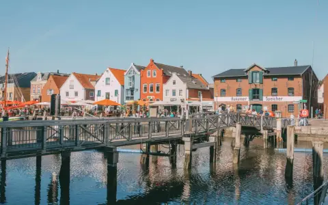 Bunte Häuser am Hafen, ein Steg führt über das Wasser. Perfekt für Ausflüge in Husum, mit Cafés und dem alten Speicher.