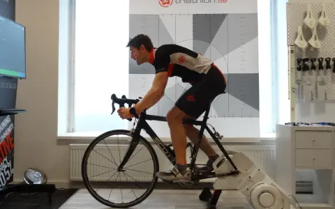 Mann auf einem Rennrad-Trainer, der sein Lungenvolumen trainiert. Hinter ihm eine Wand mit Triathlon-Logo und Messmarkierungen.